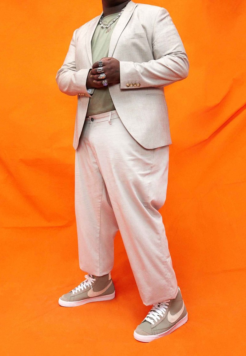 Ljusbeige kostymjacka och byxor med en lös passform; över en grön skjorta. Bärs med grå sneakers med en vit swoosh.