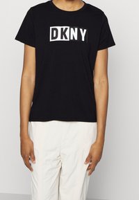 Czarny bawełniany t-shirt z białym logo "DKNY" w prostokątnym wzorze na przodzie. Krótkie rękawy i okrągły dekolt.