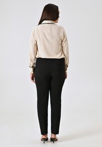 Blouse beige avec col et poignets noirs, associée à un pantalon tailleur noir et des sandales à talons noires, vue de dos.