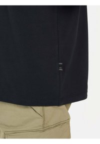Zwarte katoenen t-shirt met eenvoudige zoom, zijsplit en een klein labeldetail. Draag het met beige cargoshorts met een zijzak.