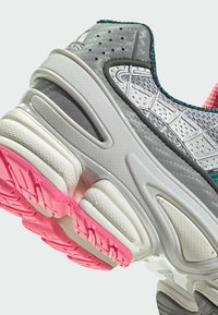 Sivi atletski tenisice s teksturiranim gornjim dijelom, ružičastim akcentima na potplatu i usnim srednjim dijelom. Imaju perforirane detalje i uzorak na dizajnu.