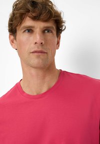 T-shirt aderente a maniche corte in cotone rosa brillante, con un classico collo a girocollo e una texture liscia. Ingrandimento dell'area del colletto.