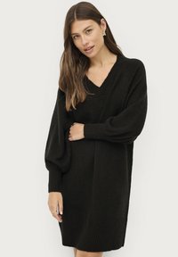 Zwart gebreid sweaterjurk met een V-hals, ballonnenmouwen en ribgebreide manchetten en zoom. Zachte textuur met een losse, ontspannen pasvorm.