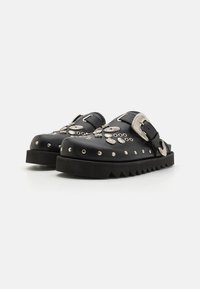 Sabots en cuir noir avec des embellissements métalliques marquants, des accents texturés et une semelle en caoutchouc dentelée pour une meilleure adhérence et stabilité.