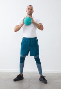 Αθλητική αρσενική φιγούρα που φοράει ένα στενό λευκό πουκάμισο και τιρκουάζ σορτς, κρατώντας μια τιρκουάζ μπάλα. Είναι εμφανή γκρι και τιρκουάζ κολάν, μαύρα παπούτσια και τατουάζ.