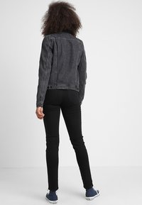 Černá džínová bunda s klasickým střihem, s límcem a zapínáním na knoflíky, doplněná černými úzkými džínami a modrými teniskami.