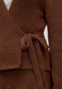 Bruine wikkelcardigan van zachte, gestructureerde brei. Heeft een strikriem in de taille en een gelaagd ontwerp met een soepele, contrasterende onderlaag.