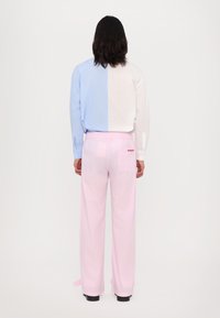 Camisa abotoada em azul claro e branco, com mangas longas; calças rosa xadrez com cintura elástica e detalhe de bolso traseiro.