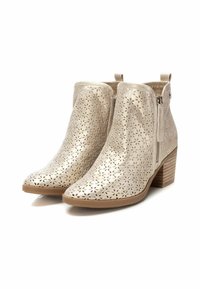 Stivali ankle beige metallizzati con motivi floreali tagliati al laser, zip laterale e tacco a blocco. Il materiale testurizzato aumenta l'interesse visivo.