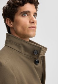Heren khaki wollen jas met een hoge kraag, voorzien van zwarte knopen en een gestructureerd ontwerp, met een zachte textuur en een getailleerde pasvorm.