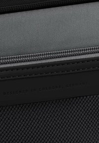 Schwarzes Stoffzubehör mit strukturiertem Oberflächmaterial, glatten Lederakzenten und einem Reißverschluss. Die Inschrift lautet "DESIGNED IN COLOGNE, GERMANY."