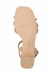 Beżowe sandały na obcasie z gładką syntetyczną cholewką, otwartym tyłem i regulowanym paskiem. Teksturowana gumowa podeszwa z detalem w postaci złotego logo.