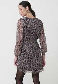 Vestido de tejido transparente con estampado floral, que presenta mangas largas, cintura elástica y una falda recogida, en tonos de morado, rosa y marrón.