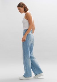 Lichtblauwe wijde spijkerbroek van denim, met een hoge taille, vijf zakken en subtiele vervaging, gecombineerd met witte sneakers.