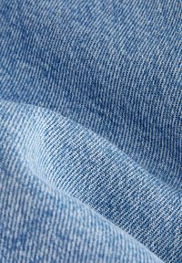 Lichtblau denimstof met een zachte textuur, met een geweven patroon en lichte kleurvariaties, wat de casual en duurzame uitstraling benadrukt.