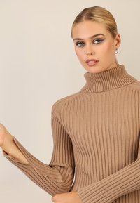 Tan ribbet turtleneck sweater med lange ærmer, der har en afslappet pasform og sideskår ved manchetterne, lavet af et blødt, tekstureret strikkemateriale.