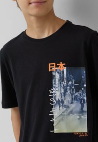 Zwarte katoenen t-shirt met een grafische print van een stadsbeeld met Japanse tekst en "TOKYO CITY LIGHTS" in oranje. Korte mouwen, ronde hals.