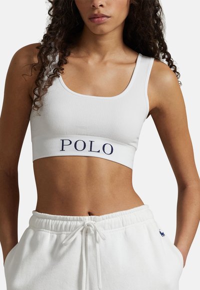 Bílý žebrovaný krátký top se širokým pruhem s nápisem "POLO" v námořnické modři. Kombinovaný s bílými tepláky s šňůrkou v pase, představujícími pohodlný střih.