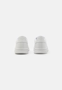 Vita sneakers med ovandel i slätt läder, vadderad krage och platt gummisula, med minimalistisk design och subtilt präglad logotyp.