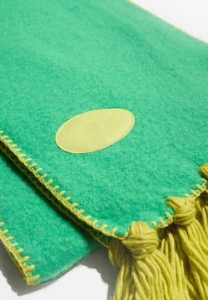 Groene wollen sjaal met gele stiksels, franjes en ovale leren patch details op een witte achtergrond.