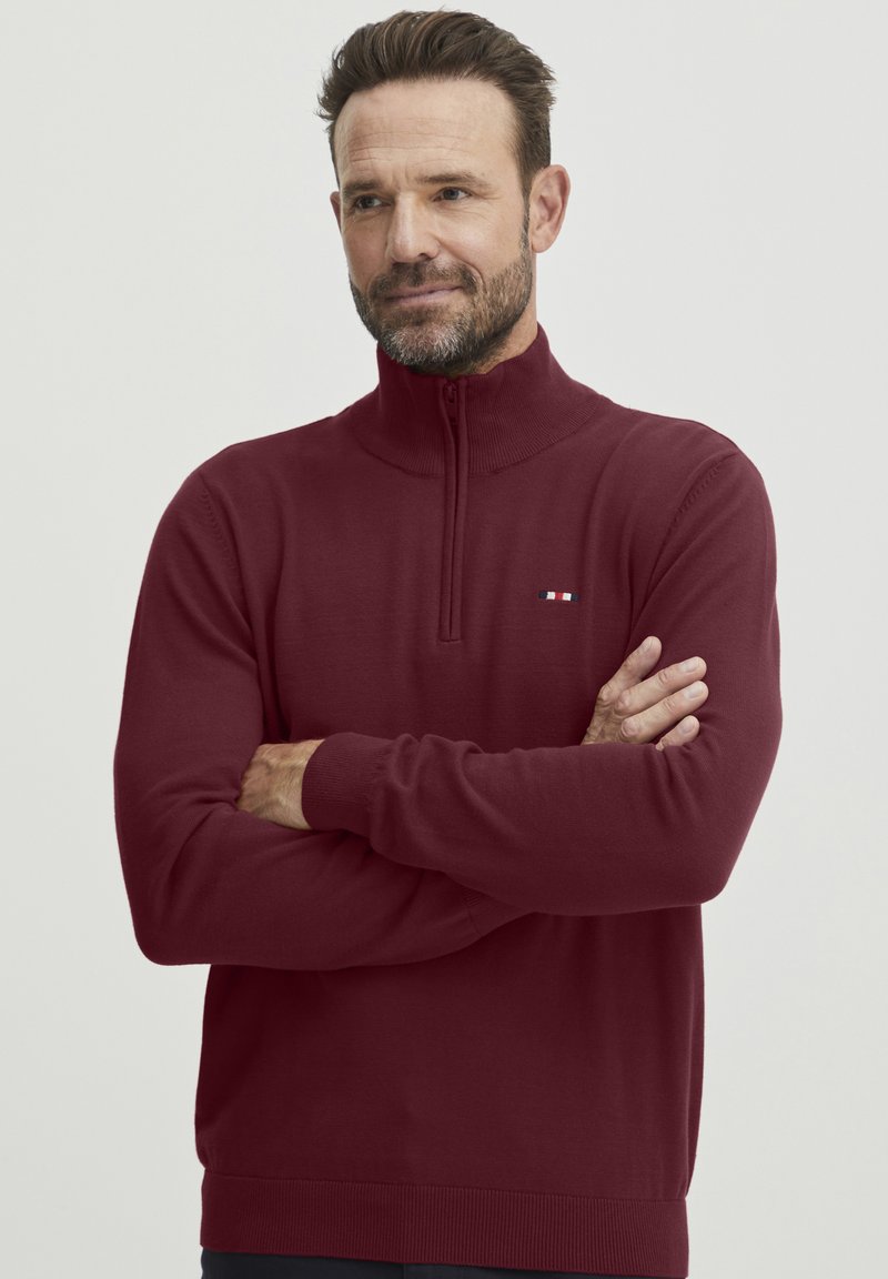 Burgundy-värinen vetoketjupaita, jossa on ribbikuvioidut hihansuut ja helma, ja vasemmassa rinnassa pieni kolmiraitainen logo. Valmistettu pehmeästä, joustavasta kankaasta.