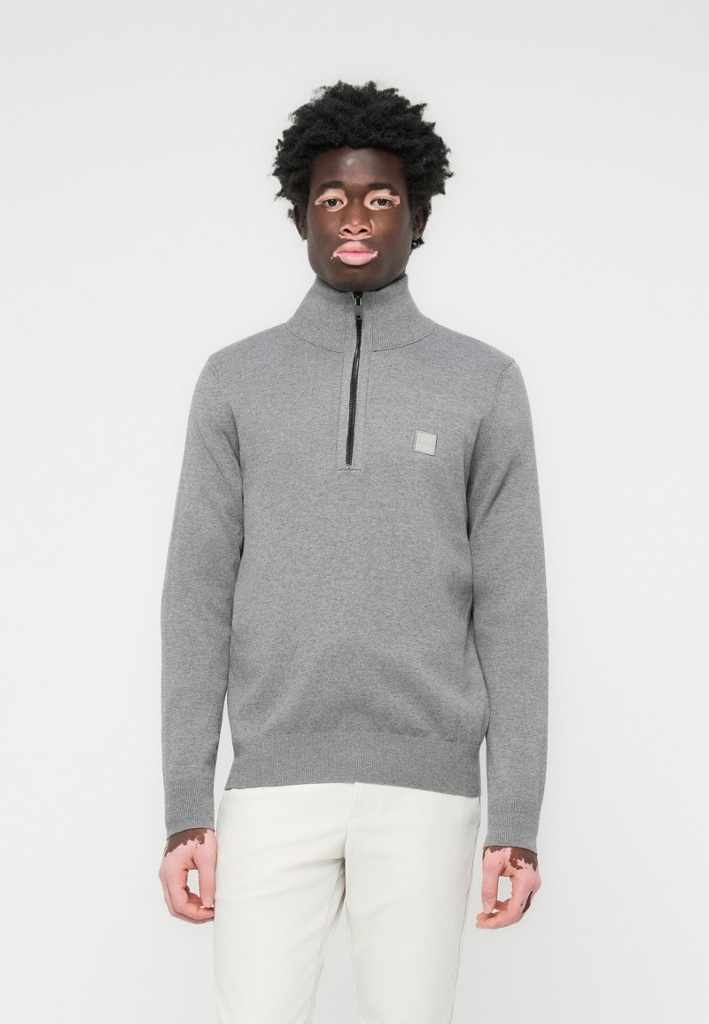 Grauer Reißverschluss-Pullover mit hohem Kragen, aus strukturiertem Stoff gefertigt, mit kleinem Logo auf der linken Brust und gerippten Bündchen und Saum.