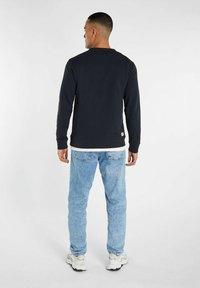 Sweat-shirt bleu marine avec un col rond et des manches longues, associé à un jean bleu clair. Le tissu semble doux ; il présente des poignets et un ourlet côtelés.
