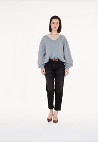 Szara, oversize bluza z dekoltem w kształcie V, podarte czarne dżinsy i szpilki w panterkę. Posiada luźny krój oraz gładką teksturę materiału.