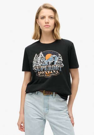 T-shirt en coton noir avec un design de montagne, des arbres, un orignal et le texte "SUPERDRY MONTANA." Manches courtes et coupe décontractée.