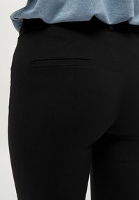 Svarta byxor gjorda av ett elastiskt tyg, med en diskret bakficka och en smal passform. Slät textur med minimal detaljering.