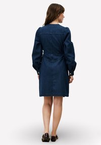 Robe en velours côtelé bleu foncé avec manches bouffantes, taille cintrée et ourlet à hauteur du genou. Présente des boutons décoratifs sur les manches et un tissu texturé.