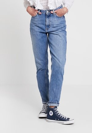 Vaqueros de mezclilla azul claro con cintura alta y corte recto. Combinados con zapatillas altas de color marino con detalles y cordones blancos.