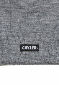 Grå strikket lue med tykk ribbestruktur og en svart etikett med hvit tekst "CAYLER." på den nedre kanten.