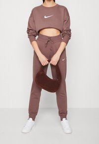 Brun cropped sweatshirt och matchande joggers med vit Nike-logotyp. Mjukt tyg, midja med dragsko. Brun fluffig väska och vita sneakers.