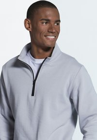 Light gray fleece pullover featuring a zippered neck, black zipper, and a soft texture, worn over a white T-shirt.