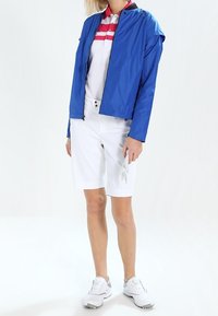 Niebieska lekka kurtka zapinana z przodu, noszona na białej i różowej, w paski, koszulce polo. W połączeniu z białymi szortami i butami golfowymi.