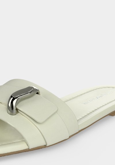 Biała skórzana klapka z zakrzywionym srebrnym metalowym detalem i wyściełaną podeszwą.