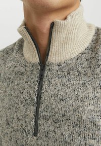 Sweter z dzianiny z wysokim kołnierzem, z pół zamkiem, teksturowany szary i beżowy materiał oraz przestrzenny wzór na całej powierzchni.