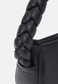 Melnā ādas rokassomu ar pītas rokturi, ar rāvējslēdzēja aizdari un gludu tekstūru. Izteikts dizains ar tīrām līnijām un minimāliem akcentiem.