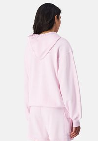 Felpa con cappuccio in cotone rosa, dal fit rilassato, con cappuccio ampio e polsini a costina, abbinata a pantaloni corti coordinati con una tasca laterale.