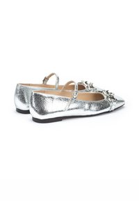 Bailarinas metálicas plateadas con una superficie texturizada. Las características incluyen una punta afilada, tiras al tobillo y lazos decorativos en la parte delantera.