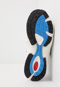 Svart gummi sula med blåa och röda accenter. Texturerad yta, vadderad design och kontrasterande vita element. Har en böjd form.