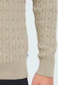 Maglione beige a coste con polsini e orlo a coste, realizzato in materiale morbido. Presenta un piccolo etichetta bianca del marchio sul lato.