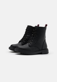 Bottes de cheville noires à lacets en cuir lisse avec bouts ronds, détails cousus et languettes contrastées au talon.