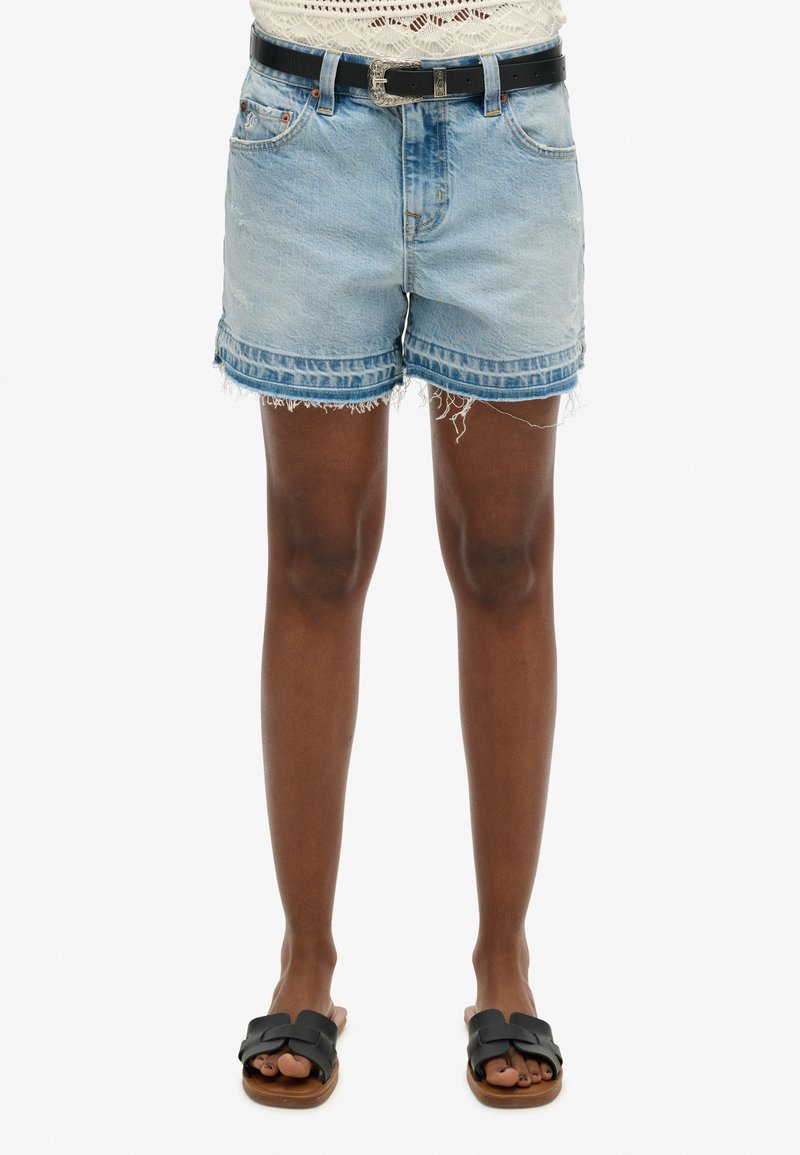 Lichtblauwe denim shorts met een rafelende zoom, vijf-pocket ontwerp en een zwarte riem. Draag ze met zwarte slide sandalen op blote voeten.