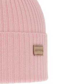 Roze gebreide muts met een geribbelde structuur en een omgevouwen boord. Aan de voorkant is een leren label zichtbaar met de tekst "LESS IS MORE" in reliëf.