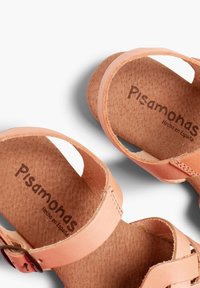Persikų spalvos odiniai šlepetės, pasižyminčios lygiu paviršiumi, plokščiomis padangomis, reguliuojamomis juostelėmis ir paminkštinta pado dalimi. Matoma "Pisamonas" prekės ženklo etiketė.