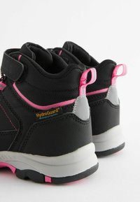 Scarpe da trekking nere con accenti rosa, in materiale impermeabile, superficie texture e supporto al tallone grigio. Cinturino in velcro per una vestibilità sicura.