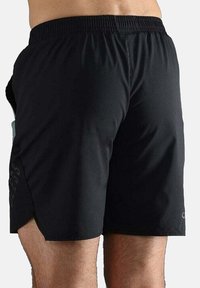 Schwarze Sportshorts aus leichtem Material, mit elastischem Bund, seitlichem Schlitz und dem Wort "fearless" auf dem linken Bein bedruckt.