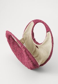 Rund, flettet håndveske i dyp rosa med en teksturert overflate og glatt beige interiør. Har to sirkulære håndtak for enkel bæring.